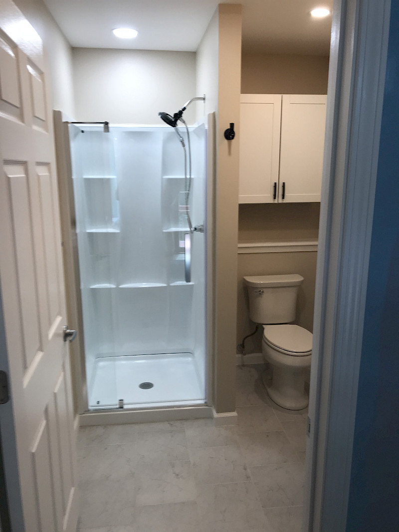 Remodeled bathroom with a white shower enclosure, glass door, tiled flooring, and a built-in storage cabinet above the toilet.