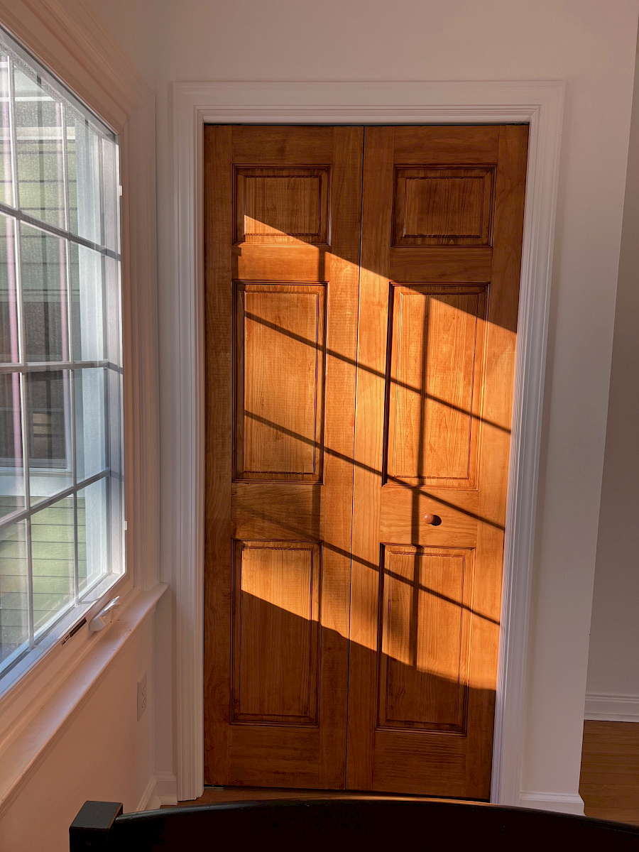 A pair of stained wood double doors framed in white trim, lit by natural light from an adjacent window.