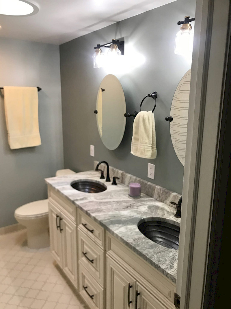 Double-vanity bathroom with hammered copper sinks, a marbled granite countertop, oval mirrors, and glass globe lighting.