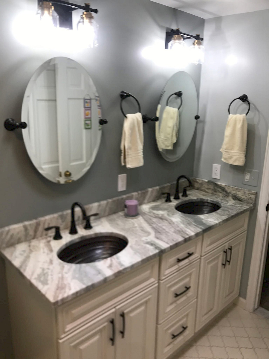 Custom double vanity with copper basin sinks, a marbled granite top, oval pivot mirrors, and antique-bronze fixtures.