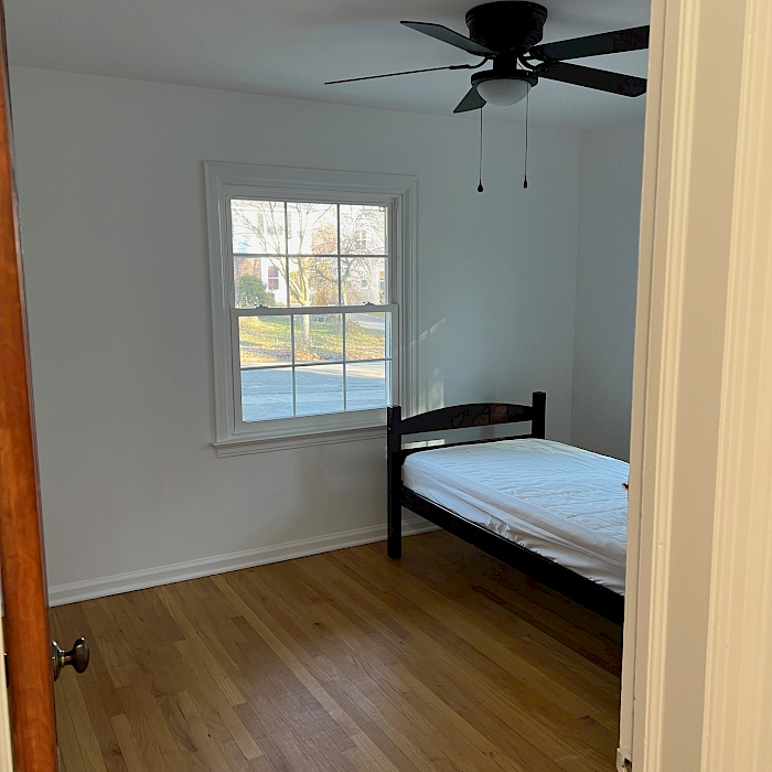 Freshly finished bedroom with refinished hardwood flooring, white window trim, and a new ceiling fan.