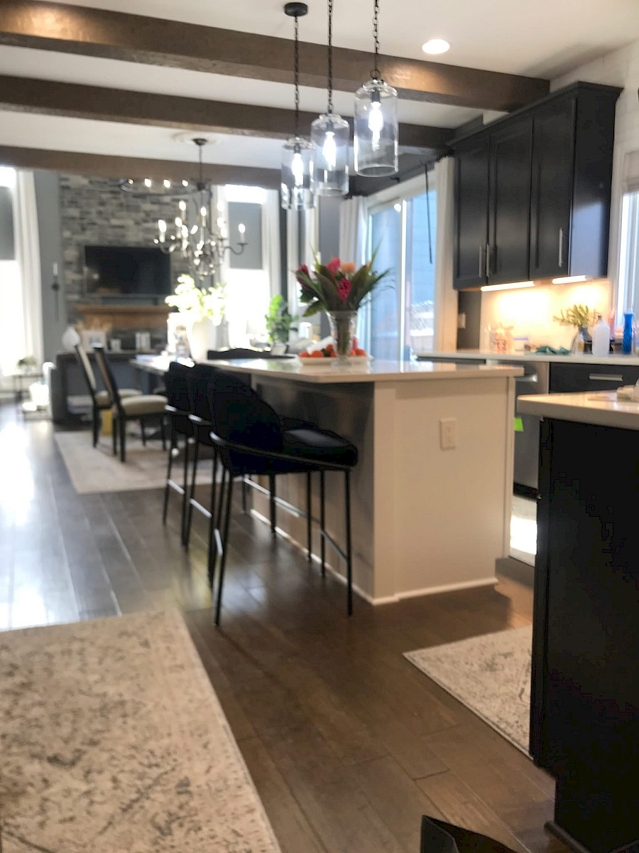 Open-concept kitchen remodel with dark shaker cabinetry, a quartz waterfall island, glass pendant lighting, and decorative wood ceiling beams.