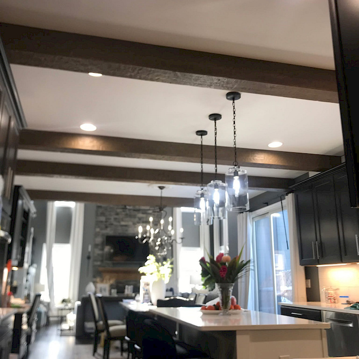 Open kitchen with a wood-beam ceiling, recessed and pendant lighting, a quartz island, and a sightline to a stone fireplace.