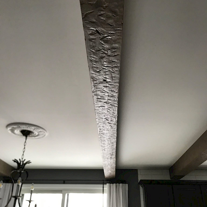 Detail of a custom rustic ceiling beam with a hand-hewn texture in a remodeled kitchen.
