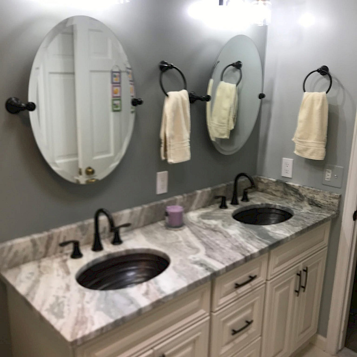 Custom double vanity with copper basin sinks, a marbled granite top, oval pivot mirrors, and antique-bronze fixtures.