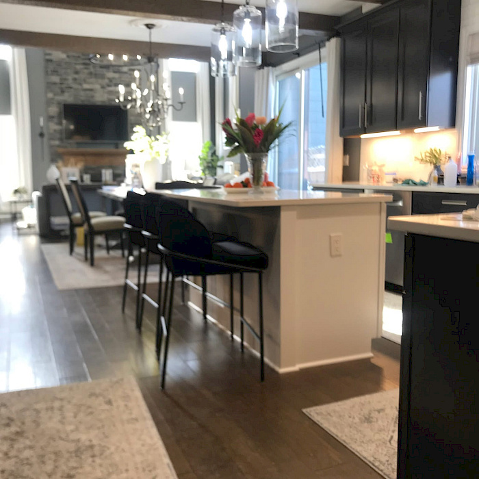 Open-concept kitchen remodel with dark shaker cabinetry, a quartz waterfall island, glass pendant lighting, and decorative wood ceiling beams.
