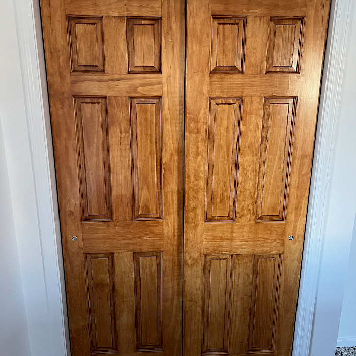 Custom-stained six-panel wood bypass closet doors finished with clean white trim.