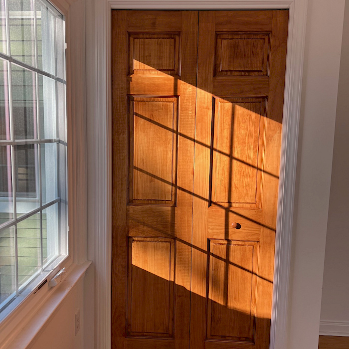 A pair of stained wood double doors framed in white trim, lit by natural light from an adjacent window.