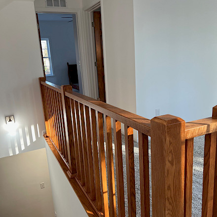 Open oak staircase with custom railing and balusters on a carpeted second-floor landing with a vaulted ceiling.