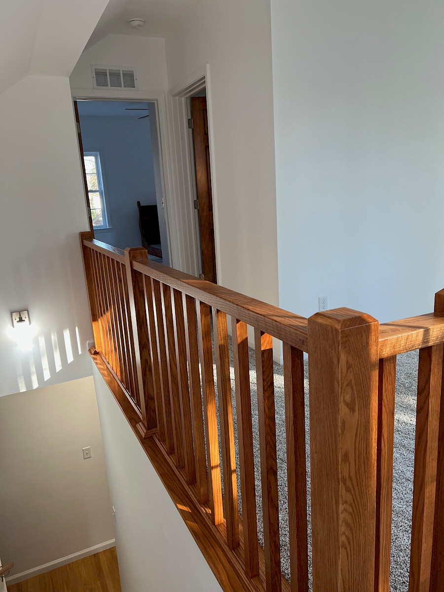 Open oak staircase with custom railing and balusters on a carpeted second-floor landing with a vaulted ceiling.